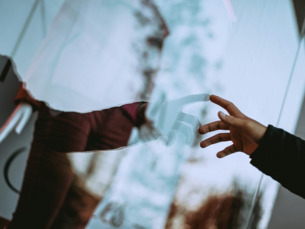 A human hand reaching towards a robotic hand reflected in glass.